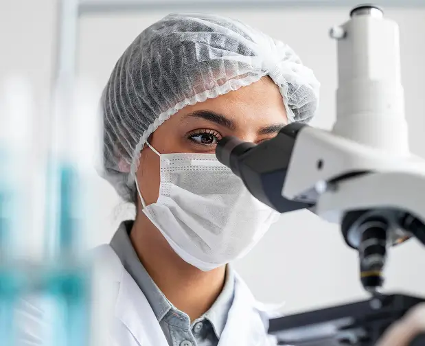 Medical researcher examining a sample through a microscope in a clinical research laboratory